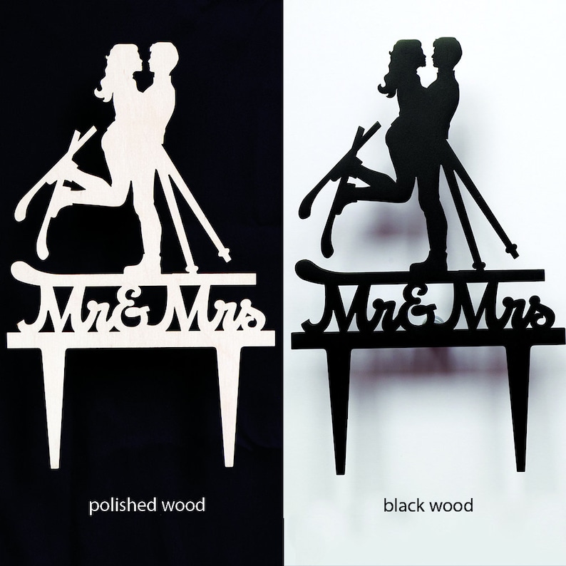 May include: Wooden wedding cake toppers in polished and black wood. The toppers feature a silhouette of a couple on skis, with the words "Mr & Mrs" below. The polished wood version is on a black background, and the black wood version is on a white background.