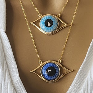 May include: Two gold necklaces with blue evil eye pendants. The top pendant has a light blue eye with a white swirl and a black center. The bottom pendant has a dark blue eye with a white swirl and a black center.