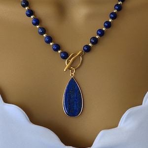 May include: A gold necklace with a teardrop-shaped lapis lazuli pendant. The necklace is made of small, round lapis lazuli beads and gold beads.
