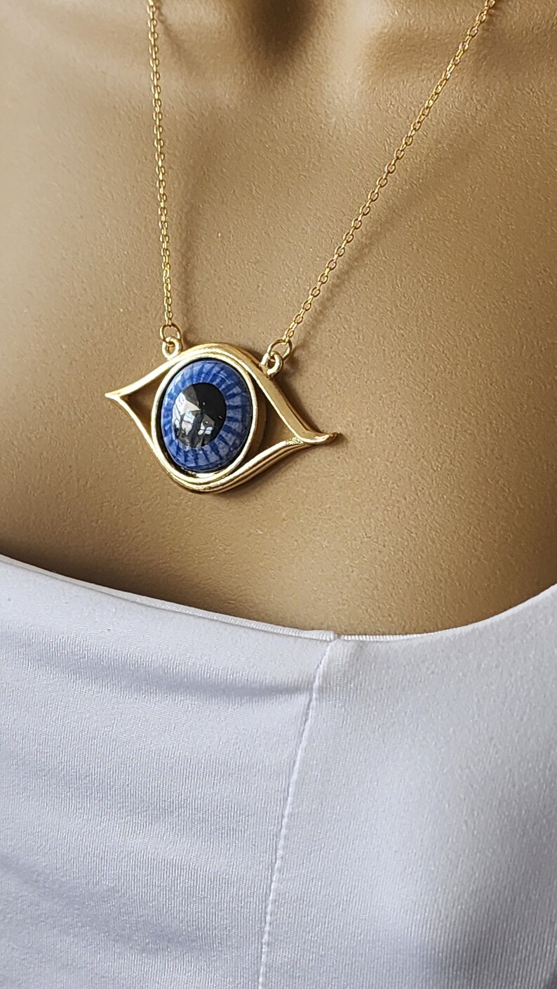 May include: A gold chain necklace with a blue evil eye pendant. The pendant is a detailed design with a gold frame and a blue eye with a black pupil.