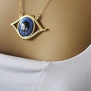 May include: Gold chain necklace with a large blue eye pendant. The eye is surrounded by a gold frame.