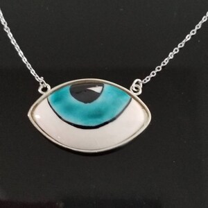 May include: A silver chain necklace with a blue and white eye pendant. The eye is surrounded by a silver frame.