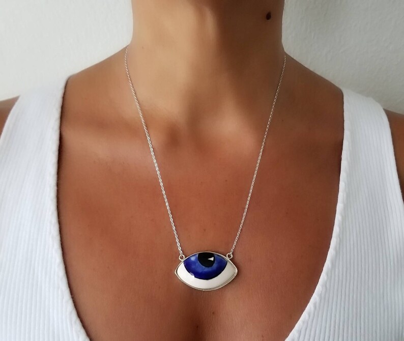 May include: A silver chain necklace with a large blue and white evil eye pendant. The pendant is shaped like an eye with a white iris and a blue pupil.