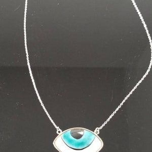 May include: A silver chain necklace with a pendant shaped like an eye. The eye is blue, white, and black.