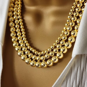 May include: A gold necklace with multiple strands of large, round beads.