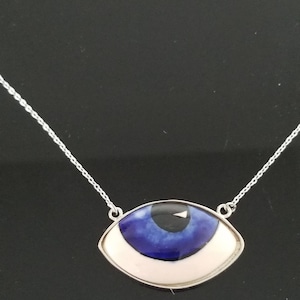 May include: A silver chain necklace with a white and blue evil eye pendant. The pendant is shaped like an eye with a blue iris and a black pupil.