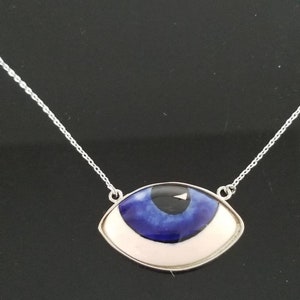 May include: A silver chain necklace with a blue and white evil eye pendant. The pendant is shaped like an eye with a white iris and a blue pupil.