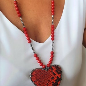 May include: A red and silver beaded necklace with a red heart-shaped pendant. The pendant has a snakeskin pattern.