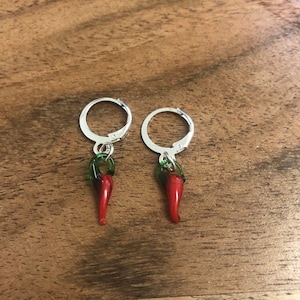 Puede incluir: Un par de pendientes de aro de plata con dijes de chile rojo y verde.
