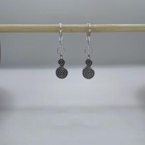 May include: A pair of silver-toned earrings with a spiral design. Each earring has a lever-back closure, a small circular accent, and a larger spiral element. The earrings are displayed on a wooden dowel against a white background.