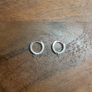 May include: Two silver hoop earrings with a small loop on the bottom of each hoop.