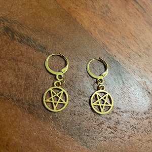 Peut inclure: Une paire de boucles d'oreilles créoles dorées avec un pendentif pentagramme suspendu à chaque créole.