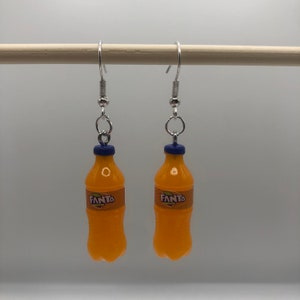 May include: A pair of orange Fanta bottle earrings with blue bottle caps and silver hooks.
