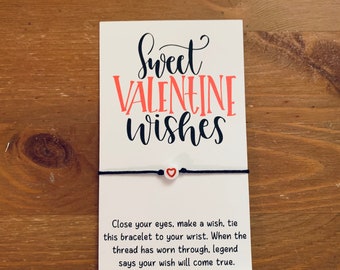 以下が含まれることがあります： 「Sweet Valentine Wishes」と黒文字で書かれた白いカード。赤いハートのついた白いビーズがついた黒い紐のブレスレットがカードにつけられています。カードには「目を閉じ、願い事をし、このブレスレットを手首に結びます。糸がすり切れたら、伝説によると願いが叶うと言われています。」と書かれています。