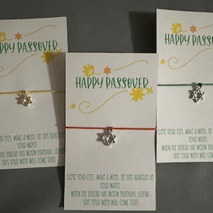 May include: Three cards with the text "Happy Passover" printed on them. Each card has a string bracelet with a silver Star of David charm attached. The cards have instructions to close your eyes, make a wish, and tie the bracelet to your wrist. When the thread wears through, legend says your wish will come true.