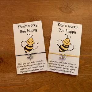 May include: Two white cards with the text "Don't worry Bee Happy" and a cartoon bee illustration. Each card has a silver charm bracelet with a bee charm attached.