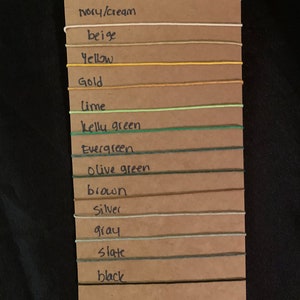 May include: A color chart with 14 different colors of string, including white, ivory, beige, yellow, gold, lime, kelly green, evergreen, olive green, brown, silver, gray, slate, and black.