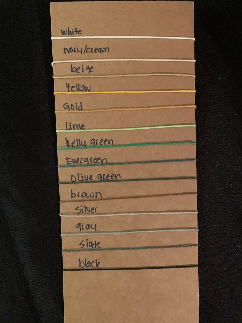 May include: A color chart with 14 different colors of string, including white, ivory, beige, yellow, gold, lime, kelly green, evergreen, olive green, brown, silver, gray, slate, and black.