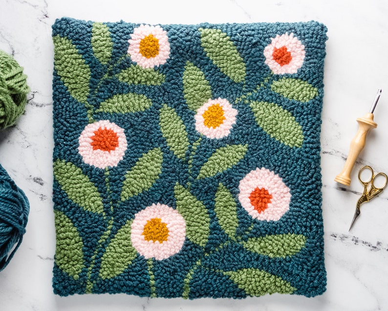 May include: A teal blue hand-stitched cushion with a floral design. The flowers are pink, orange, and yellow. The cushion is made with a wool blend and is perfect for adding a touch of handmade charm to any room.