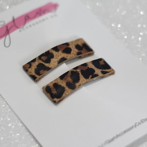 Puede incluir: Dos pinzas para el pelo rectangulares de color marr&oacute;n y negro con estampado de leopardo. Las pinzas tienen una ligera curva.