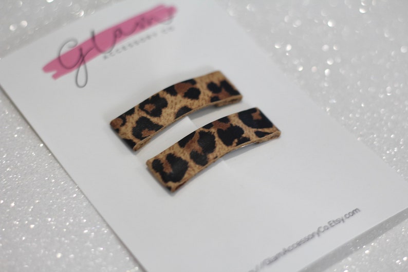 Puede incluir: Dos pinzas para el pelo rectangulares de color marr&oacute;n y negro con estampado de leopardo. Las pinzas tienen una ligera curva.