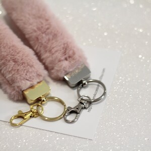 May include: Two fluffy pink keychains with gold and silver key rings. The keychains are made of faux fur and have a small metal charm attached to the top.