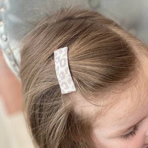 Puede incluir: Primer plano del cabello de un ni&ntilde;o con una peque&ntilde;a pinza para el pelo de estampado de leopardo blanco y rosa.