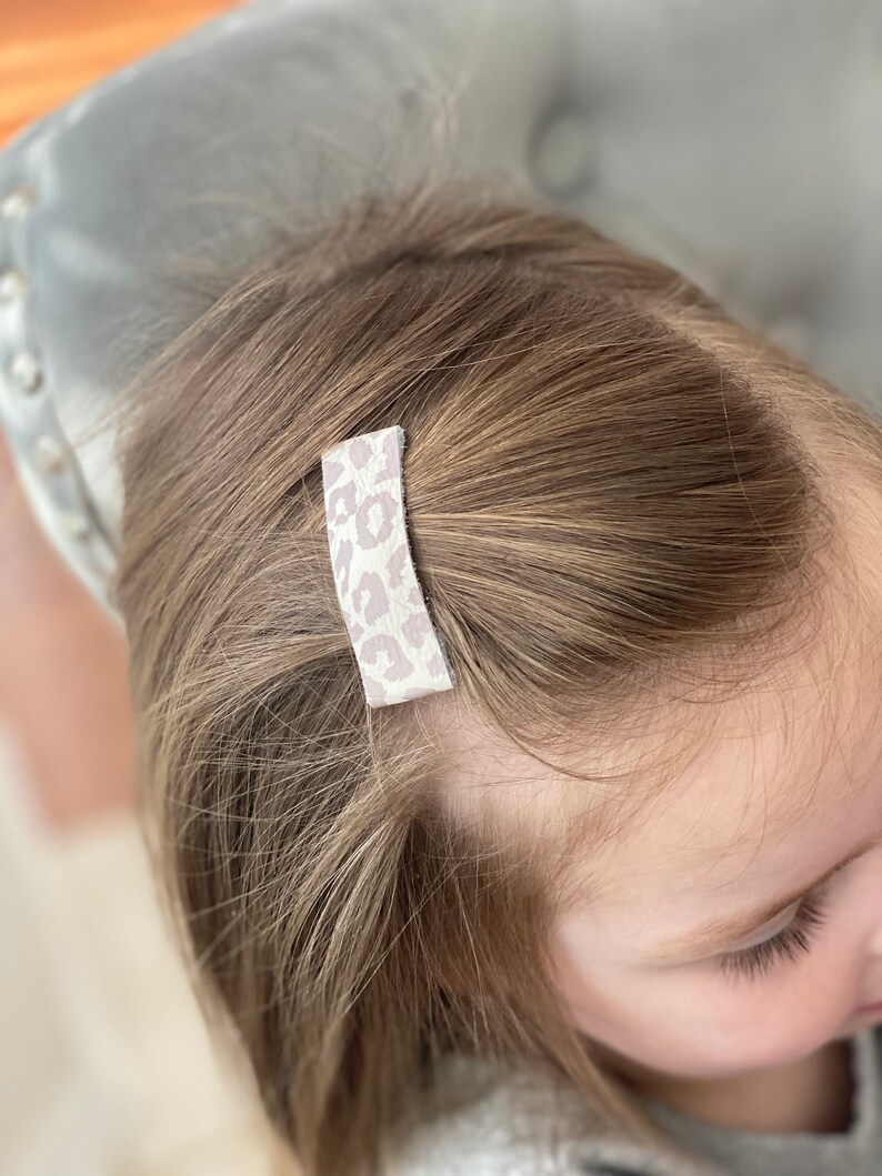 Puede incluir: Primer plano del cabello de un ni&ntilde;o con una peque&ntilde;a pinza para el pelo de estampado de leopardo blanco y rosa.