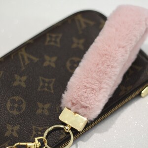 May include: A pink faux fur keychain charm attached to a gold key ring and a brown and gold zippered pouch.