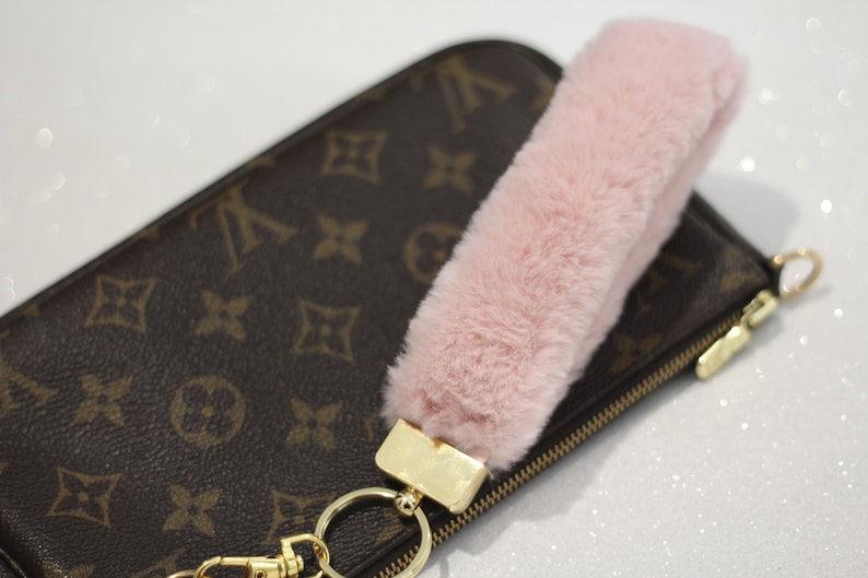 May include: A pink faux fur keychain charm attached to a gold key ring and a brown and gold zippered pouch.
