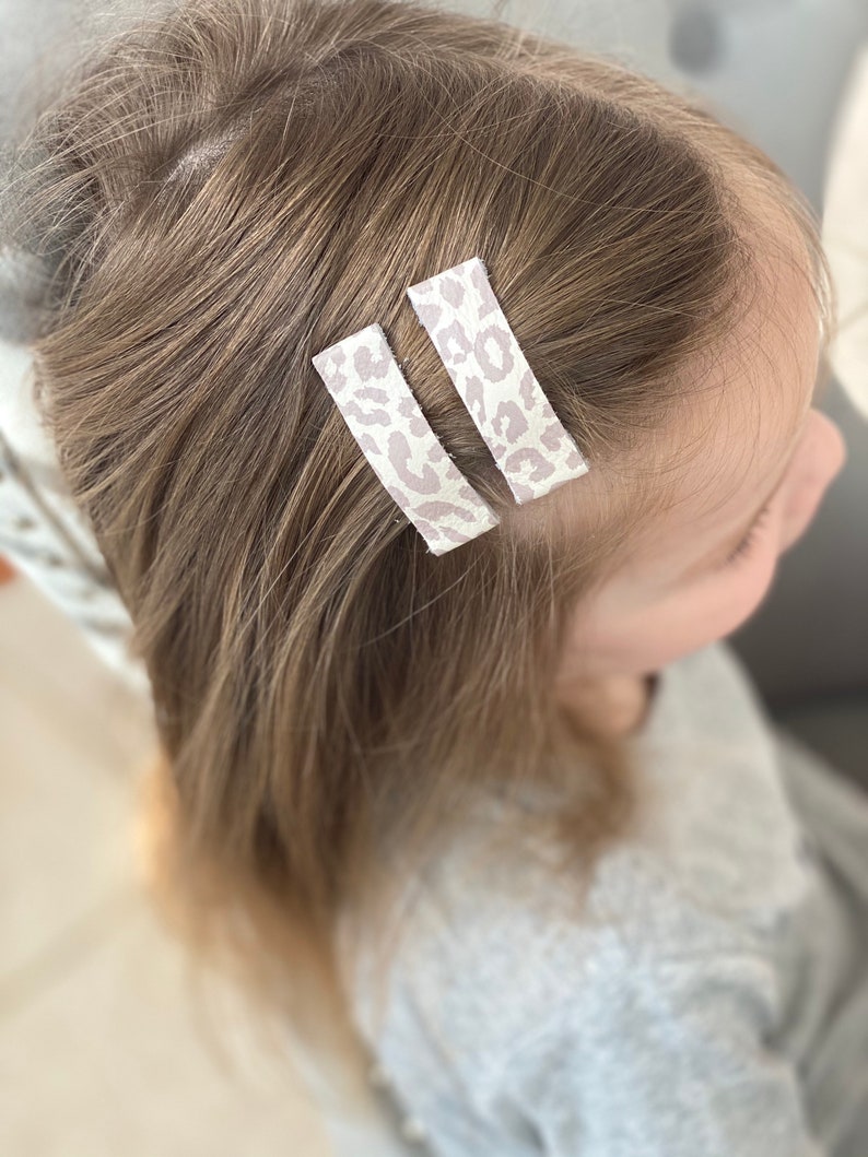 Puede incluir: Dos peque&ntilde;as pinzas para el pelo con un dise&ntilde;o de estampado de leopardo en tonos blancos y marrones claros.