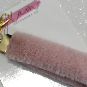 May include: A pink fluffy keychain with a gold key ring and a gold metal connector. The keychain has the text "Glam Accessory Co" on a white background.