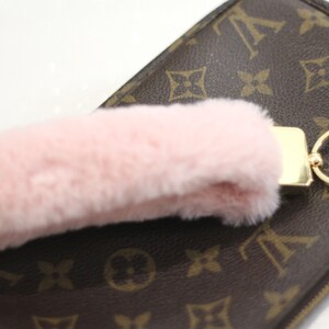 May include: A pink fluffy keychain charm attached to a gold key ring and a brown leather purse with a monogram pattern.