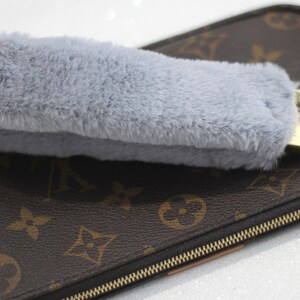 May include: A grey faux fur keychain charm attached to a gold key ring and a brown leather purse with a gold zipper.
