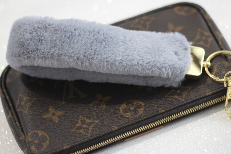 May include: A grey faux fur keychain charm attached to a gold key ring and a brown leather purse with a gold zipper.