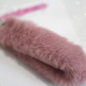 May include: A soft, pink, fluffy keychain with a silver key ring.