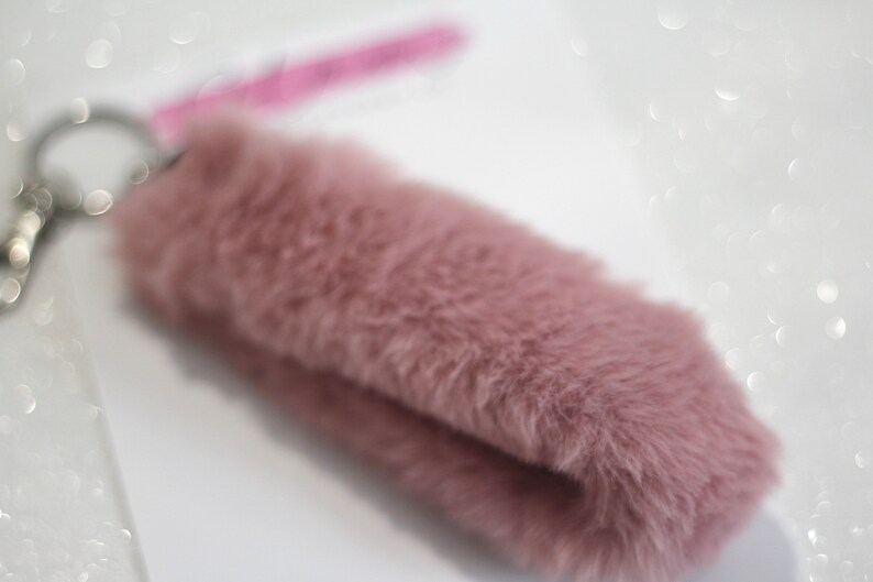 May include: A soft, pink, fluffy keychain with a silver key ring.