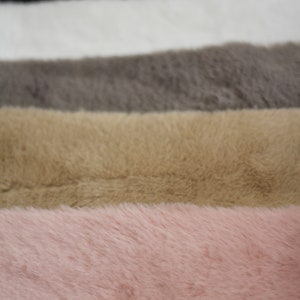 May include: Five different colours of faux fur fabric swatches. The swatches are arranged in a stack, with the black swatch on top and the pink swatch on the bottom. The swatches are all the same size and shape.