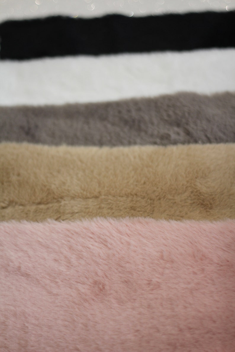 May include: Five different colours of faux fur fabric swatches. The swatches are arranged in a stack, with the black swatch on top and the pink swatch on the bottom. The swatches are all the same size and shape.