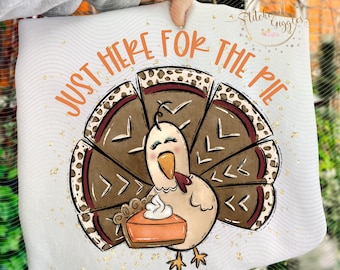 May include: White Thanksgiving-themed pillow with a cartoon turkey holding a pumpkin pie. The text "JUST HERE FOR THE PIE" is in orange. The turkey has a red wattle and is surrounded by brown and tan feathers.