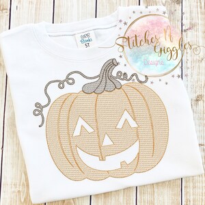 May include: A white t-shirt with an embroidered orange pumpkin with a jack-o-lantern face. The text "Stitches N Giggles Designs" is embroidered on the shirt.