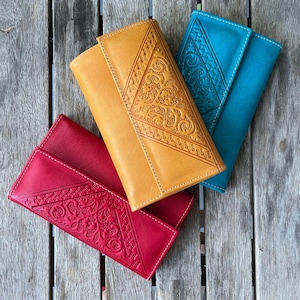 Peut inclure: Trois portefeuilles rectangulaires en cuir de couleur jaune moutarde, rouge vif et bleu sarcelle. Chaque portefeuille présente un rabat triangulaire avec un motif floral gaufré complexe et une bordure géométrique, avec fermeture à rabat.