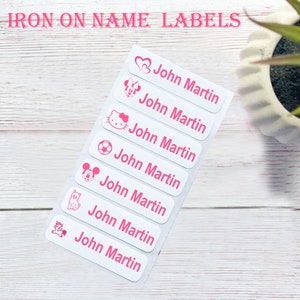 May include: Seven white iron-on name labels with pink outlines and various pink icons. The labels read "John Martin".