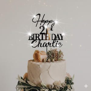 K&ouml;nnte beinhalten: Eine Geburtstagstorte mit einem schwarzen Acryl-Kuchenaufsatz mit der Aufschrift "Happy 21st Birthday Charlie". Die Torte ist mit Blumen und Gr&uuml;n geschm&uuml;ckt. Die Torte hat ein wei&szlig;es Frosting.