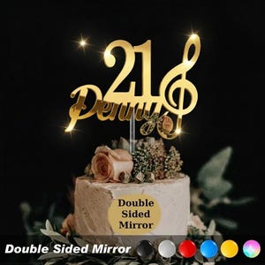 May include: A gold-coloured cake topper featuring the number "21" and a treble clef design. The name "Penny" is written in cursive. The topper sits atop a cake decorated with flowers. The words "Double Sided Mirror" are also visible on the image.