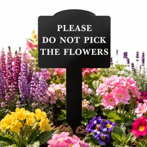 May include: A black rectangular garden sign with a pointed stake featuring the white text PLEASE DO NOT PICK THE FLOWERS, positioned in a garden bed filled with vibrant yellow, pink, purple, and magenta primrose and lavender flowers.
