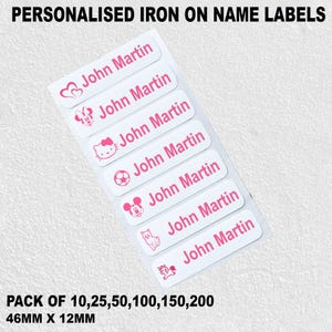 May include: A sheet of white iron-on name labels with pink text and graphics. Each label says "John Martin" and has a different design, such as hearts and cartoon characters. The labels measure 4.6cm x 1.2cm.