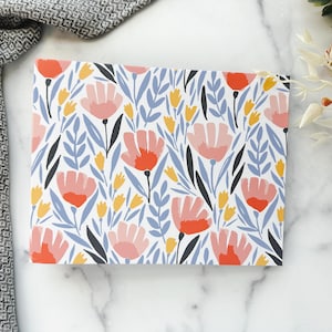 May include: A rectangular notebook with a floral pattern. The design features pink and orange flowers, yellow buds, and blue leaves on a white background. Black stems and leaves complete the design. The notebook is on a marble surface.