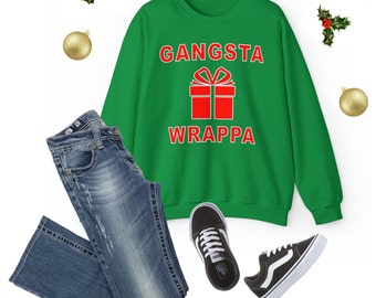 Pode incluir: Camisola de Natal verde com o texto "Gangsta Wrappa" em letras vermelhas e uma caixa de presente vermelha com um laço branco.