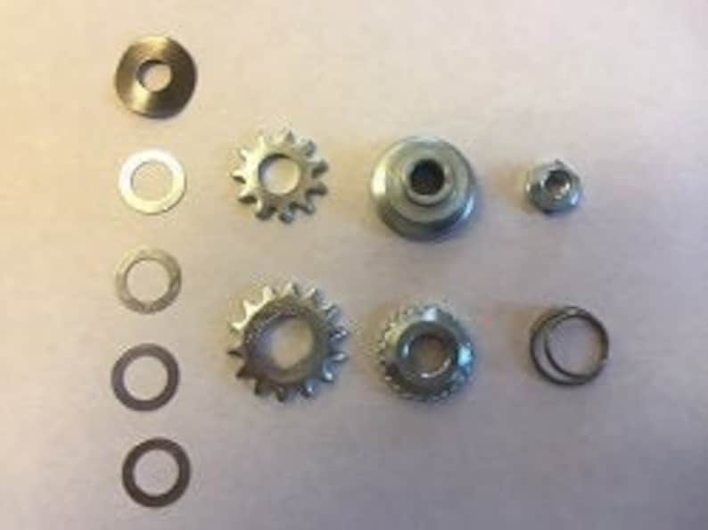 May include: A set of silver-toned metal gears and washers. The set includes two large gears, two small gears, and four washers.